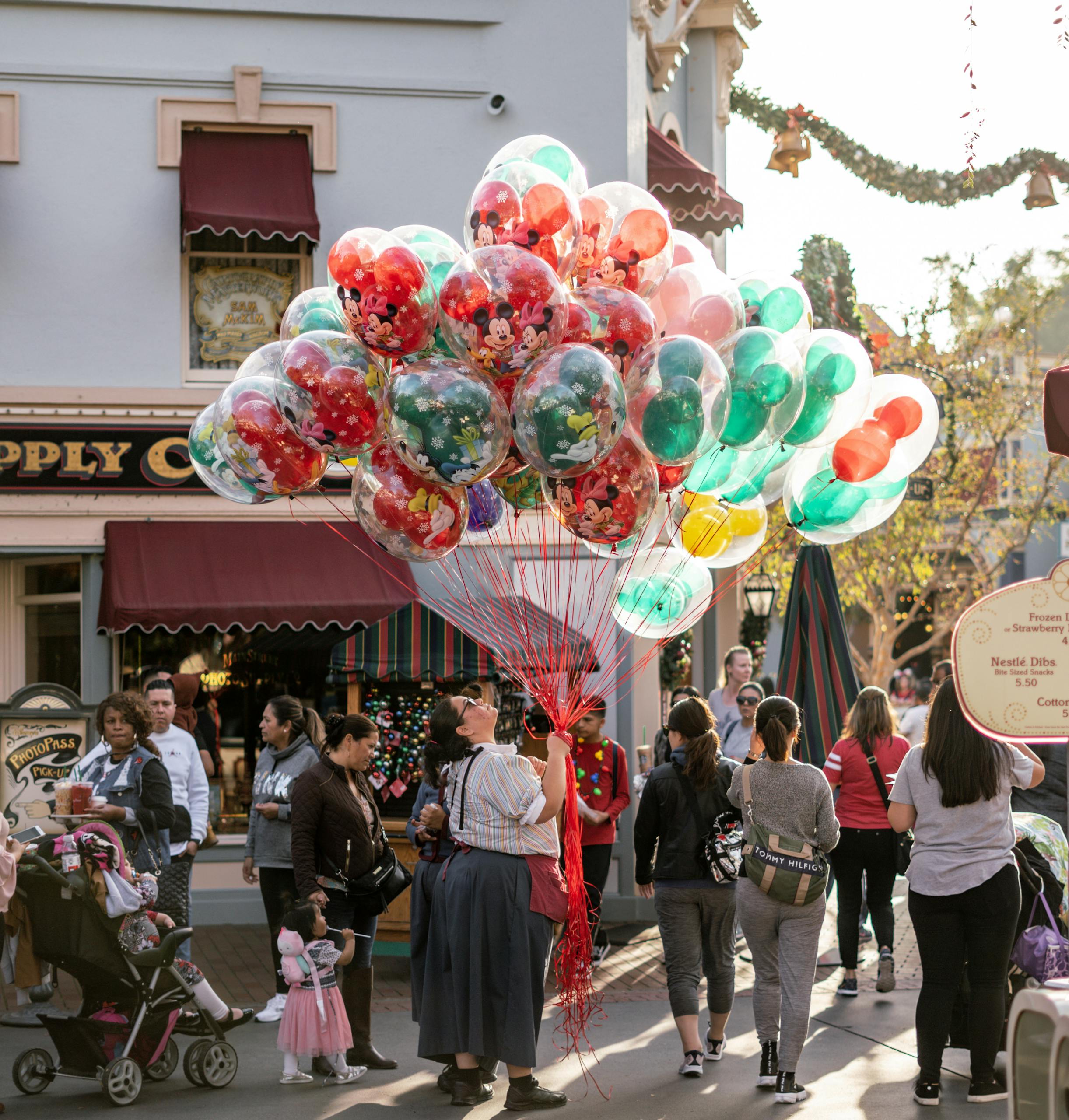 A lively street scene featuring a vendor selling vibrant balloons amidst a bustling crowd during daytime festivities.