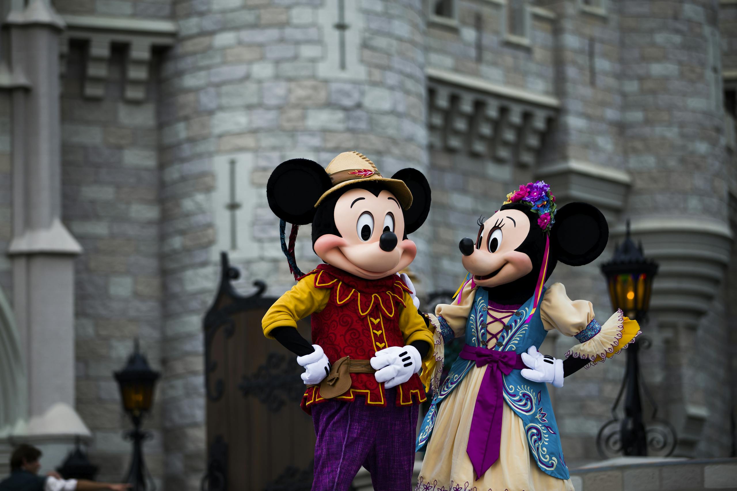 Mickey and Minnie Mouse in colorful costumes outside an iconic castle setting.