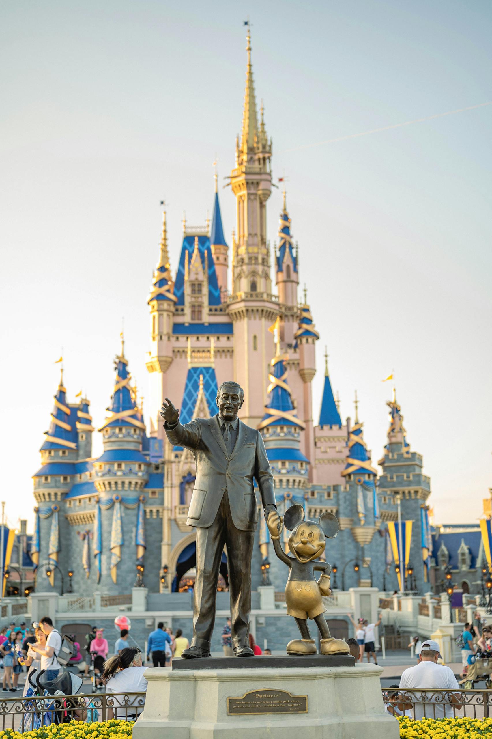 Walt Disney statue and Cinderella Castle at Disney World with evening light.