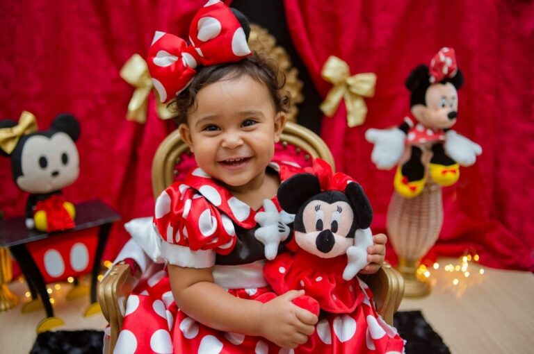 Little girl in a red and white polka dot dress with Mickey ears holding a Minnie ears holding a Minnie mouse doll