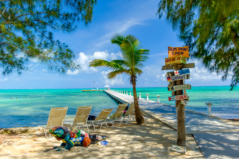 Caribbean scene with beach chairs on a small beach next to a pier and a colorful sign