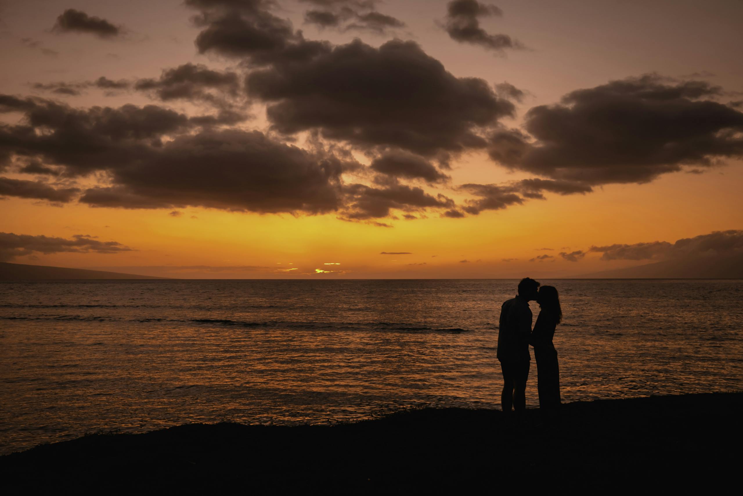 A couple shares a kiss in silhouette against a breathtaking Lahaina sunset over the ocean.