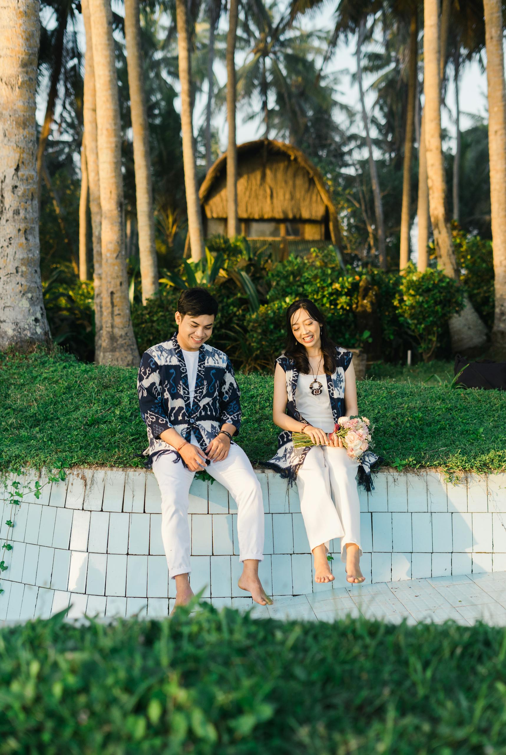 Smiling couple sitting in a tropical garden, surrounded by palm trees and greenery.
