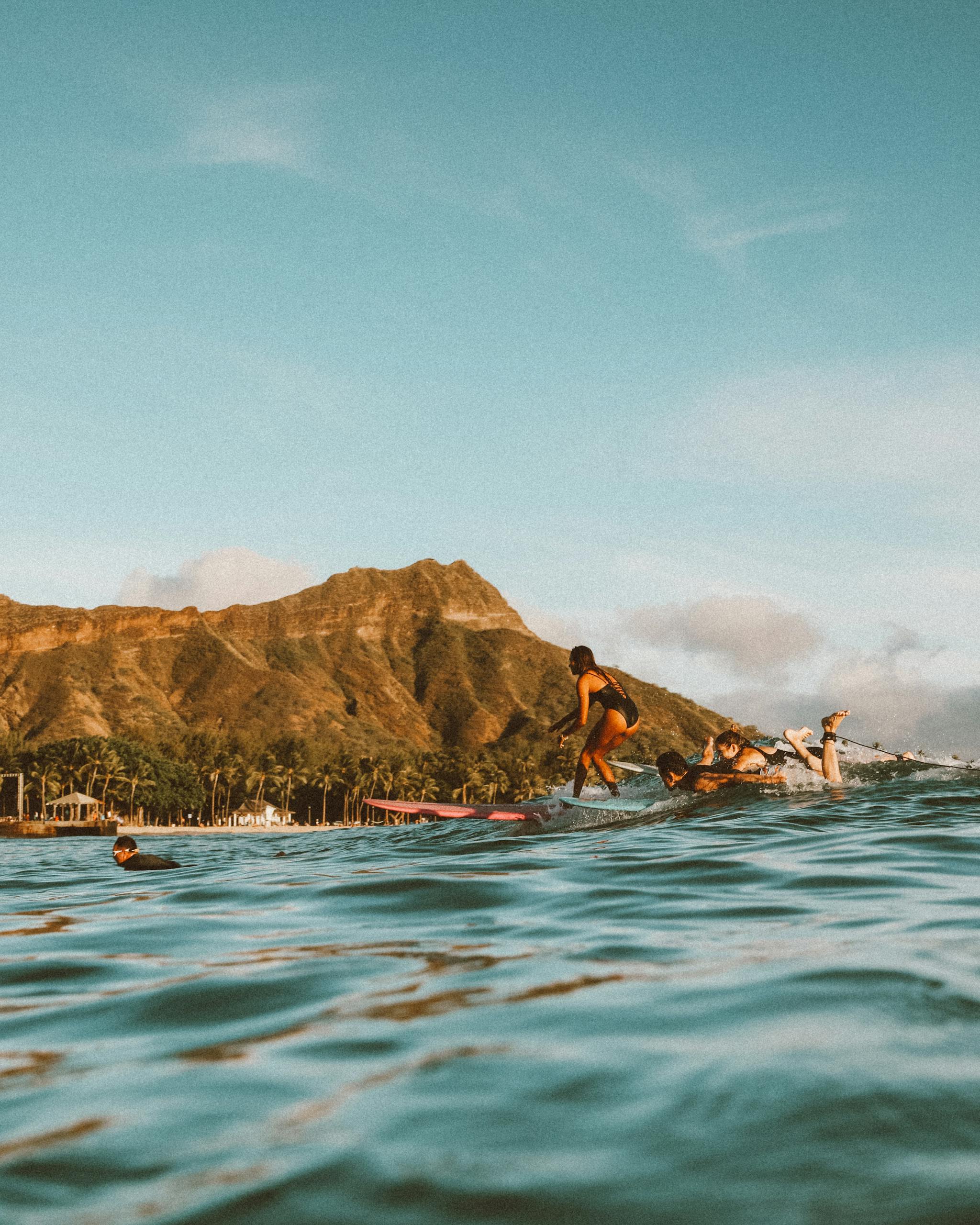 Surfers catch waves near Diamond Head on a sunny day in Hawaii, showcasing an island paradise.