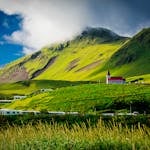 Beautiful landscape of a red-roofed church nestled in lush green hills under a vibrant sky in Iceland.