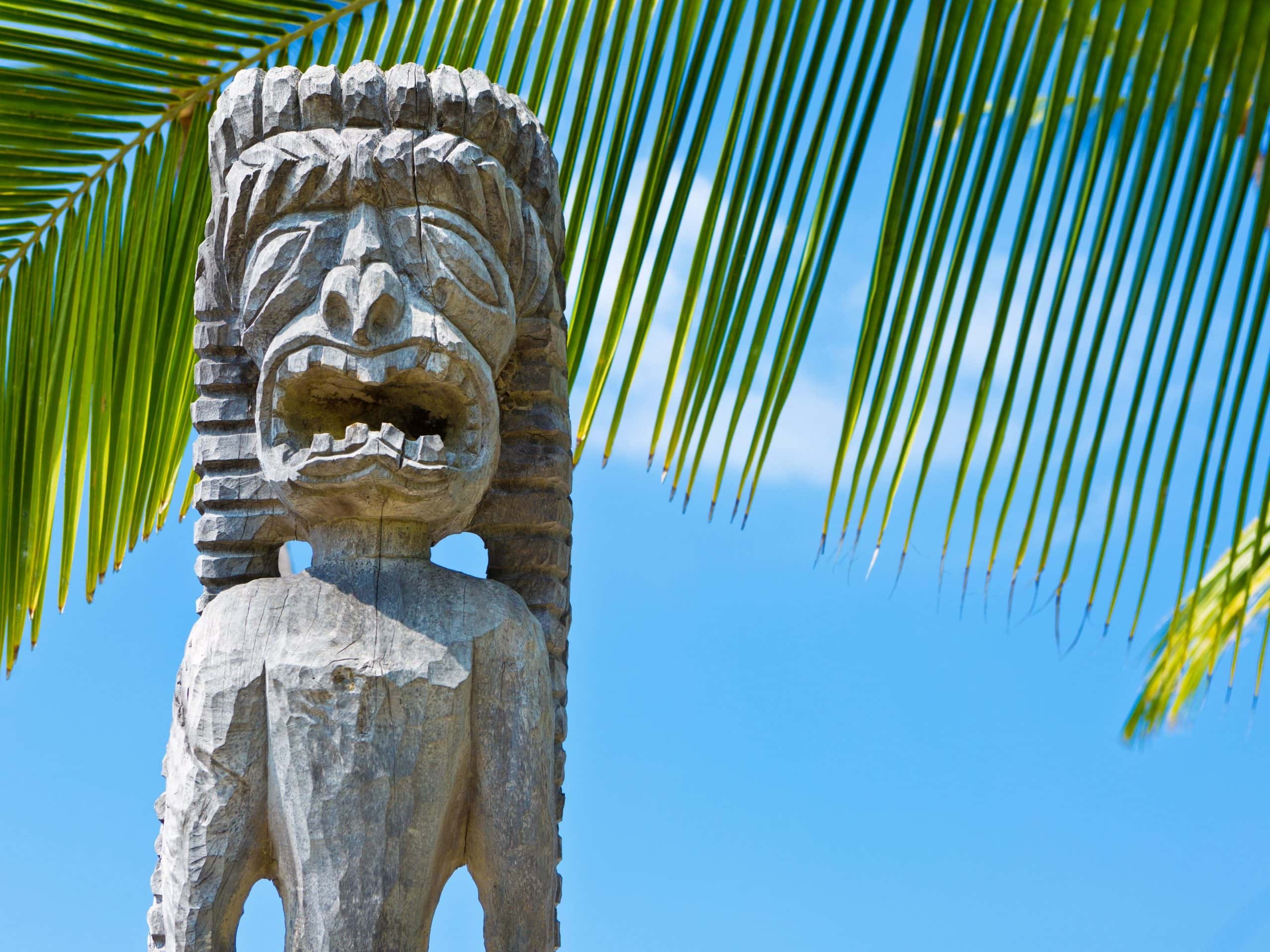 An Ancient Wooden Hawaiian Carving In Front of A Palm Tree.
